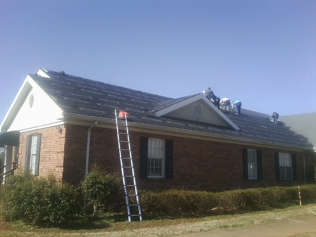 Crew tearing shingles off a brick ranch roof with a ladder set — Emergency Roof Repair work by our crew in Hendrum