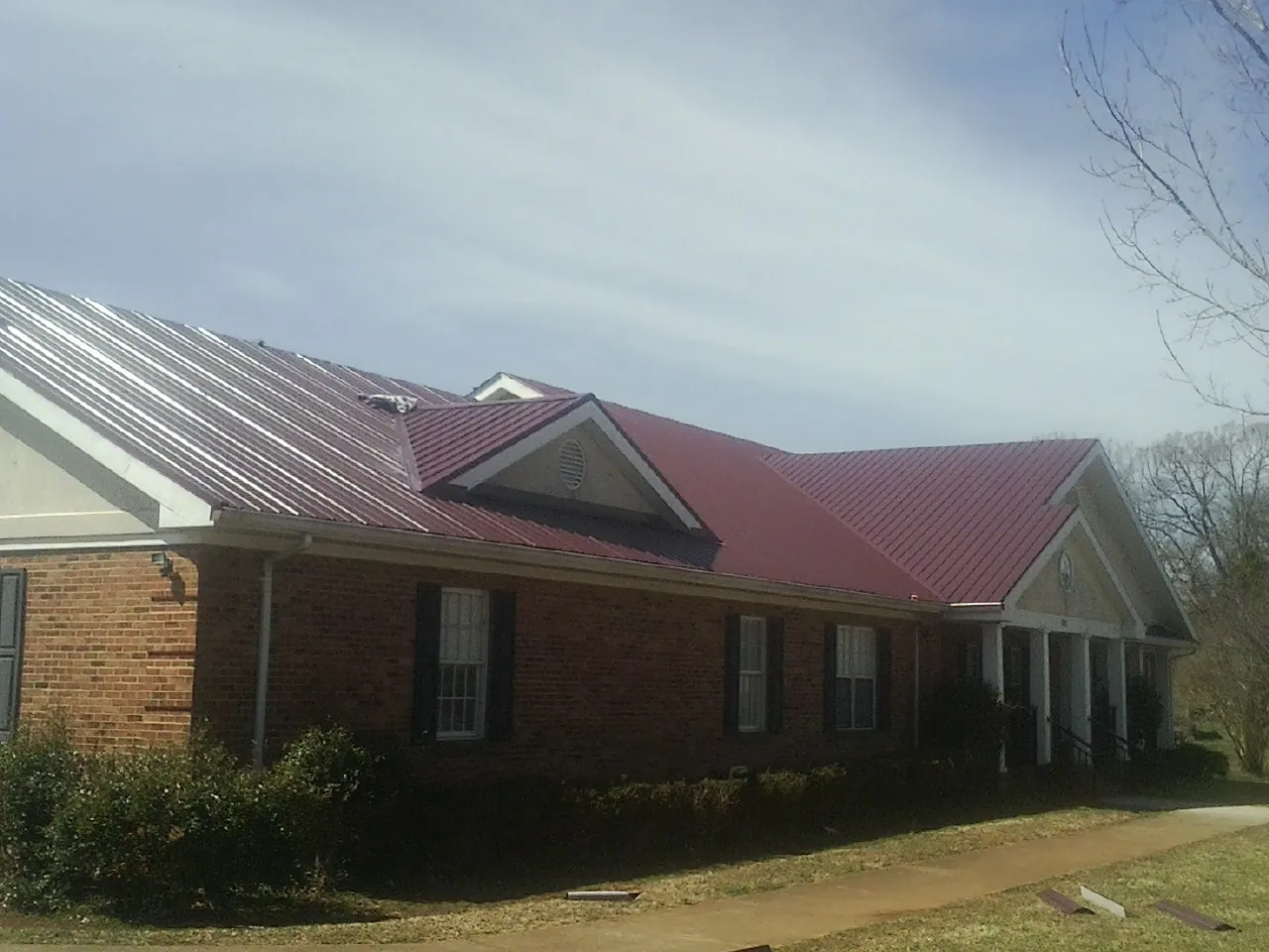 Red metal roof with gabled entries on a long brick building, from a Hail Damage Roof Repair job in Hendrum
