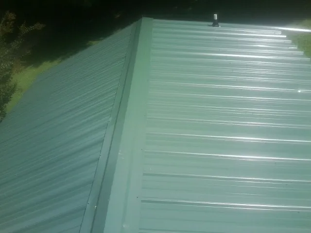 New green metal panels meeting at the ridge of a roof — Flat Roof Repair work by our crew in Hendrum