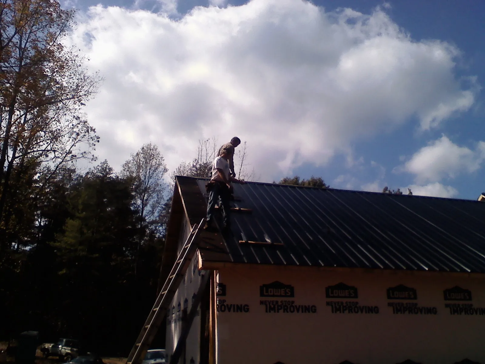 Roofer fastening dark metal panels high against a cloudy sky, from a Roof Inspection job in Hendrum
